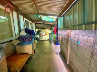 A covered corridor leading to an open area with various household items.