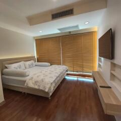 Modern bedroom with large bed, wooden blinds, and wall-mounted TV