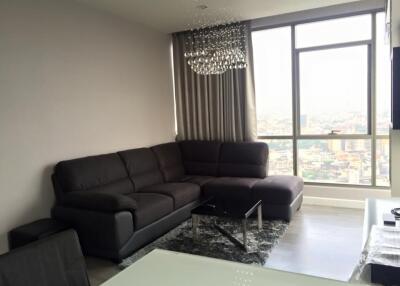 Modern living room with large window, grey sectional sofa, chandelier, and city view