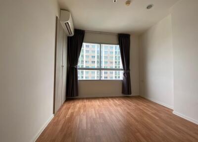 Empty bedroom with wooden floors, window with curtains, and air conditioner