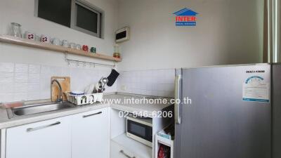 Small kitchen with white cabinets, stainless steel sink, microwave, and refrigerator