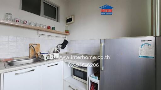 Small kitchen with white cabinets, stainless steel sink, microwave, and refrigerator