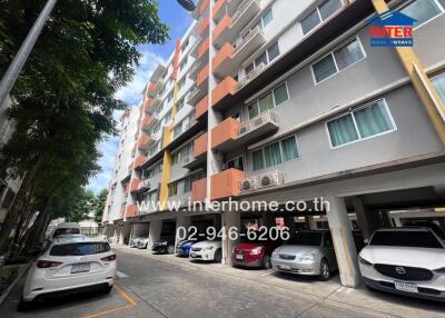 Exterior view of multi-story residential building with parking area and vehicles