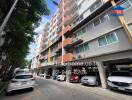 Exterior view of multi-story residential building with parking area and vehicles