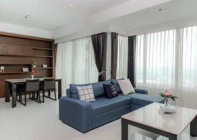 Living room with blue sectional sofa, coffee table, large windows, and dining area