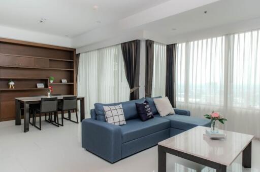 Living room with blue sectional sofa, coffee table, large windows, and dining area