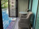 Balcony with wicker chairs and a small table overlooking a swimming pool