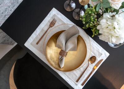 Elegantly set dining table with gold plate, napkin, cutlery, and flower arrangement