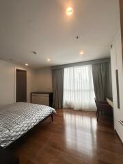 Spacious bedroom with wooden flooring, bed, desk and chair, and large window with curtains