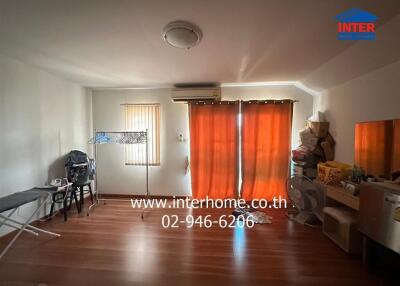 Bedroom with wooden floor, red curtains, air conditioner, and various personal items