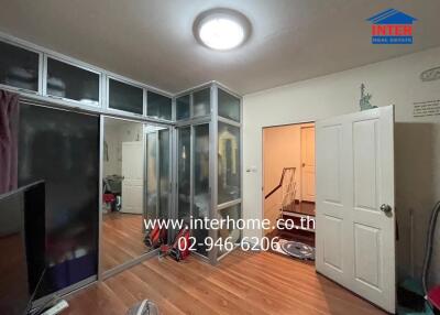 Interior view of a bedroom with wooden flooring, a mirrored wardrobe, and an open door leading to another room.