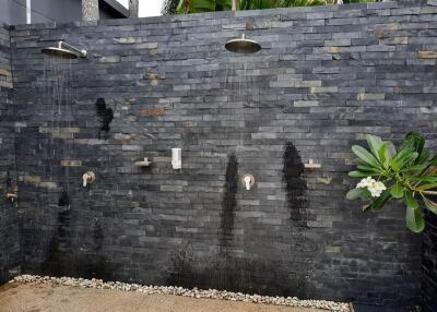 Outdoor shower area with two rainfall showerheads and a dark stone wall