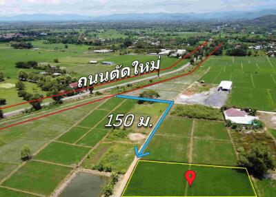 Aerial view of a plot of land marked with a pin, adjacent to a road and surrounded by green fields