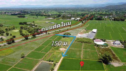 Aerial view of a plot of land marked with a pin, adjacent to a road and surrounded by green fields