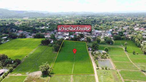 Aerial view of a plot of green land marked by boundaries, with surrounding fields and a village in the background