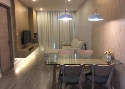 Modern living room and dining area with a cozy sofa, wall-mounted TV, dining table, and chairs.