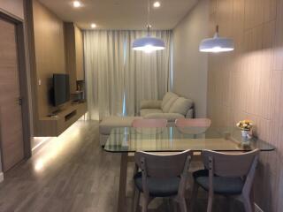 Modern living room and dining area with a cozy sofa, wall-mounted TV, dining table, and chairs.