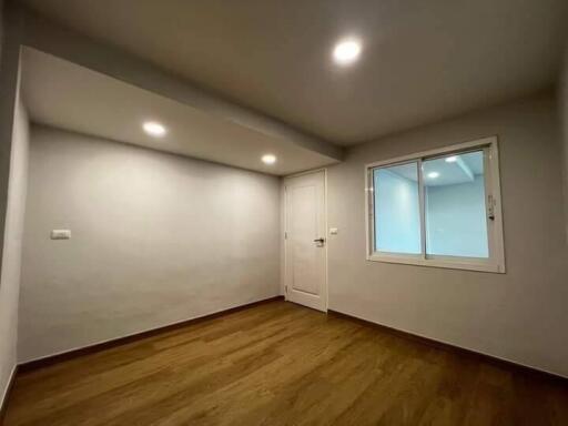 Minimalist bedroom with wooden flooring, a window, and a white door