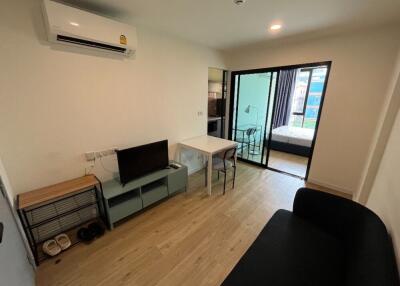 Modern living area with a TV, small table, and adjoining bedroom