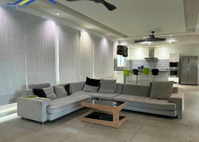 Spacious living room with gray sectional sofa, ceiling fan, and view of a modern kitchen.