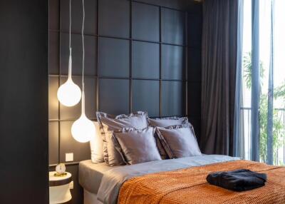 Modern bedroom with a large bed, dark paneled wall, pendant lights, and floor-to-ceiling windows.