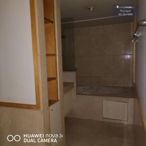 A bathroom with beige tiles, a bathtub, built-in shelves, and a dual camera photo notice.