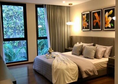 Spacious modern bedroom with large windows, framed artwork, and cozy bedding