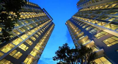 Tall modern apartment buildings with illuminated windows at dusk.