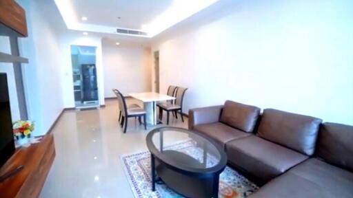 Modern living room with brown leather sofa, glass coffee table, and dining area