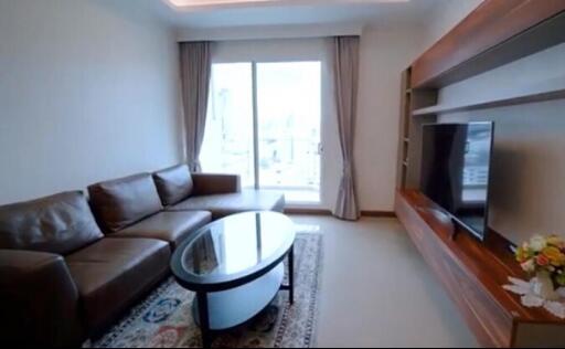 Modern living room with a large brown leather sectional sofa, a glass coffee table, a flat-screen TV on a wooden media console, and large sliding glass doors leading to a balcony.