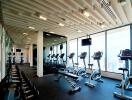 Modern fitness center with cardio machines, weights, and large windows