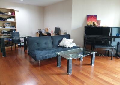 Modern living room with black sofa, glass table, shelves, and piano