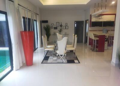 Modern dining area with glass table and stylish high-back chairs, adjacent to kitchen with red accents