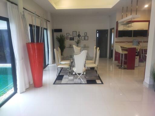 Modern dining area with glass table and stylish high-back chairs, adjacent to kitchen with red accents