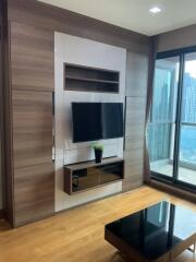 Modern living room with large windows, wooden flooring, and a mounted TV.