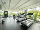 Well-equipped gym with multiple treadmills and weight machines, featuring a scenic view of greenery