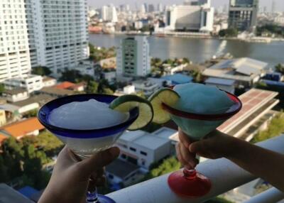 Two people holding drinks on a balcony with a city view