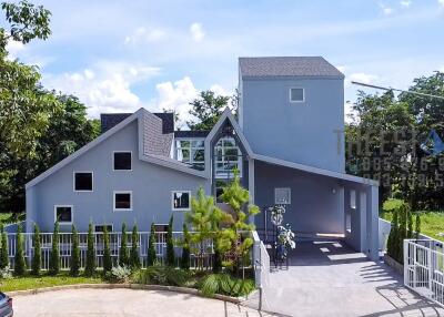 Exterior view of a modern grey house with multiple gables and lush surroundings