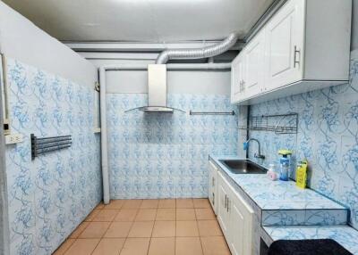 Kitchen with tiled walls and floor, cabinetry, sink, range hood, and cleaning supplies