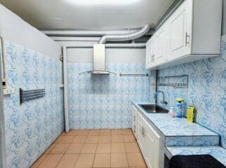 Kitchen with tiled walls and floor, cabinetry, sink, range hood, and cleaning supplies