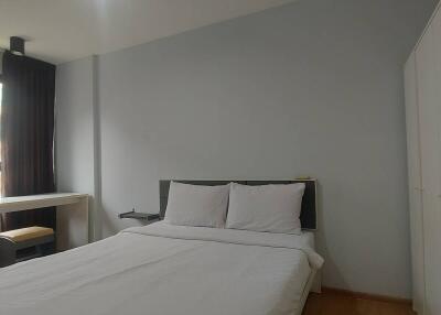 A well-lit bedroom with a bed, wardrobe, chair, desk, and a window.