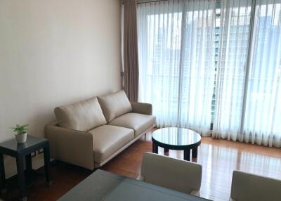 Modern living room with a beige sofa and a coffee table, featuring large windows with sheer curtains