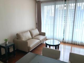 Modern living room with a beige sofa and a coffee table, featuring large windows with sheer curtains