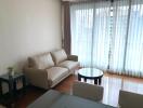 Modern living room with a beige sofa and a coffee table, featuring large windows with sheer curtains