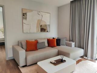 Modern living room with a grey couch, orange and checkered pillows, abstract wall art, coffee table, and floor-to-ceiling curtains.