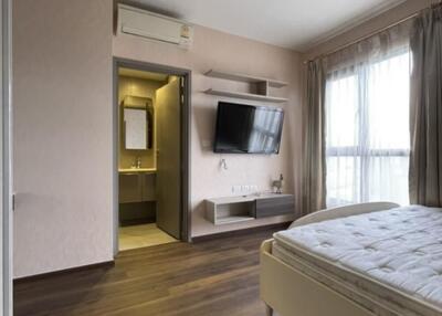 Bedroom with wooden flooring, large window, mounted TV, and attached bathroom