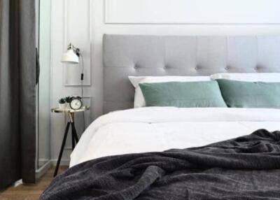 Modern bedroom with grey upholstered headboard, green pillows, a sleek lamp, and a small side table with an alarm clock