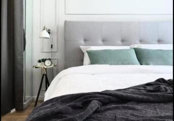 Modern bedroom with grey upholstered headboard, green pillows, a sleek lamp, and a small side table with an alarm clock