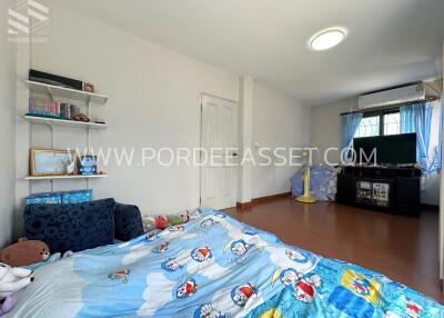 Spacious bedroom with a bed covered in cartoon-themed bedding, a blue armchair, bookshelf, and television.