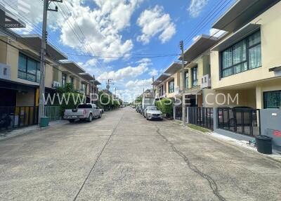 A view of the neighborhood with modern townhouses lining a clean street under a blue sky with some clouds.